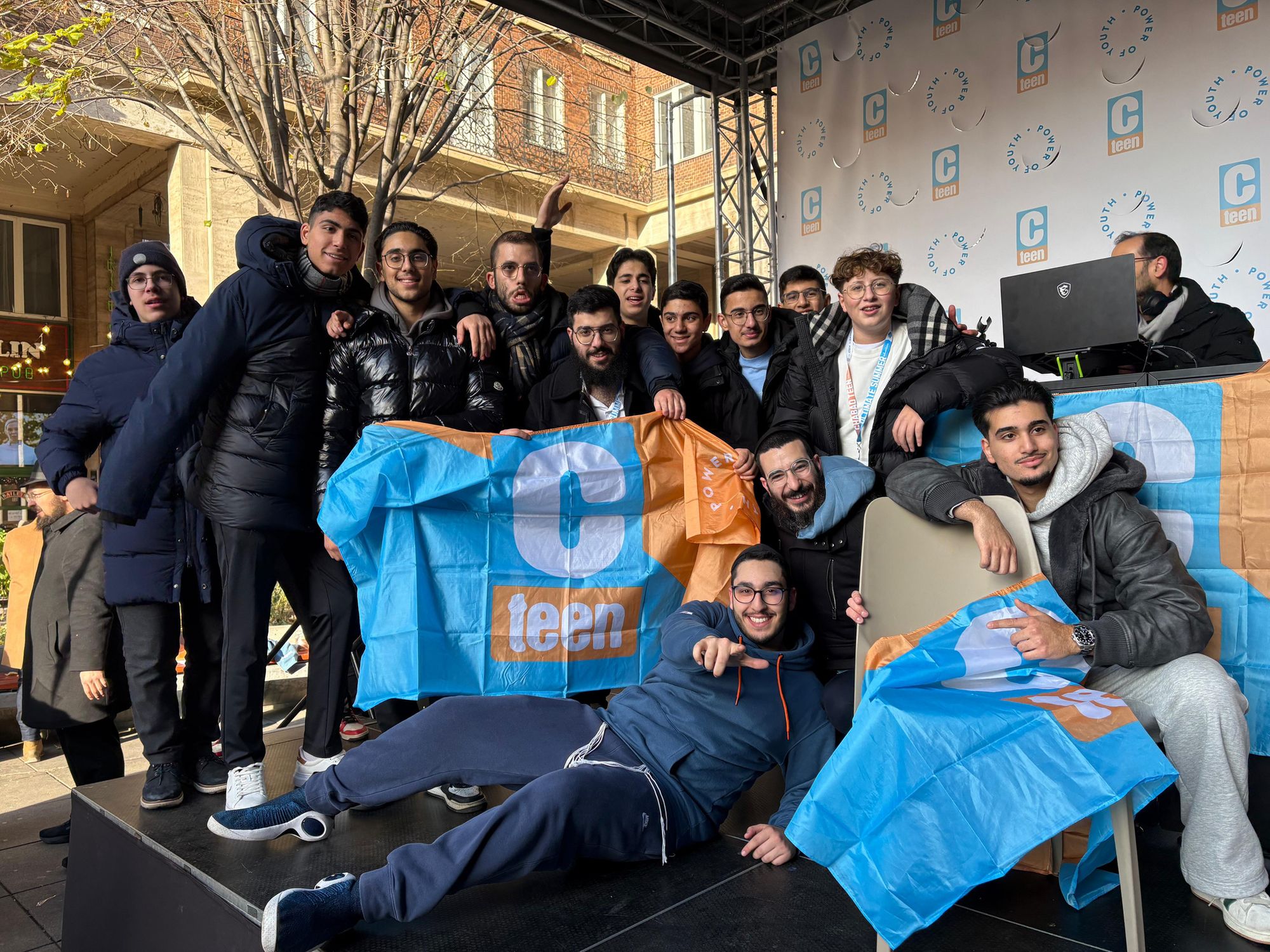 A group of Club Chai teenagers together outdoors in Vienna, smiling and holding CTeen banners.